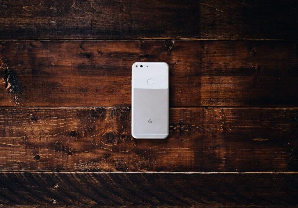 A white and gray phone laying face down on a brown wood surface.