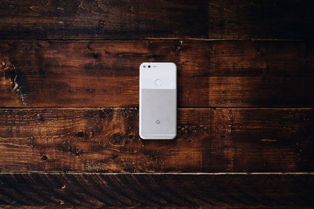 A white and gray phone laying face down on a brown wood surface.